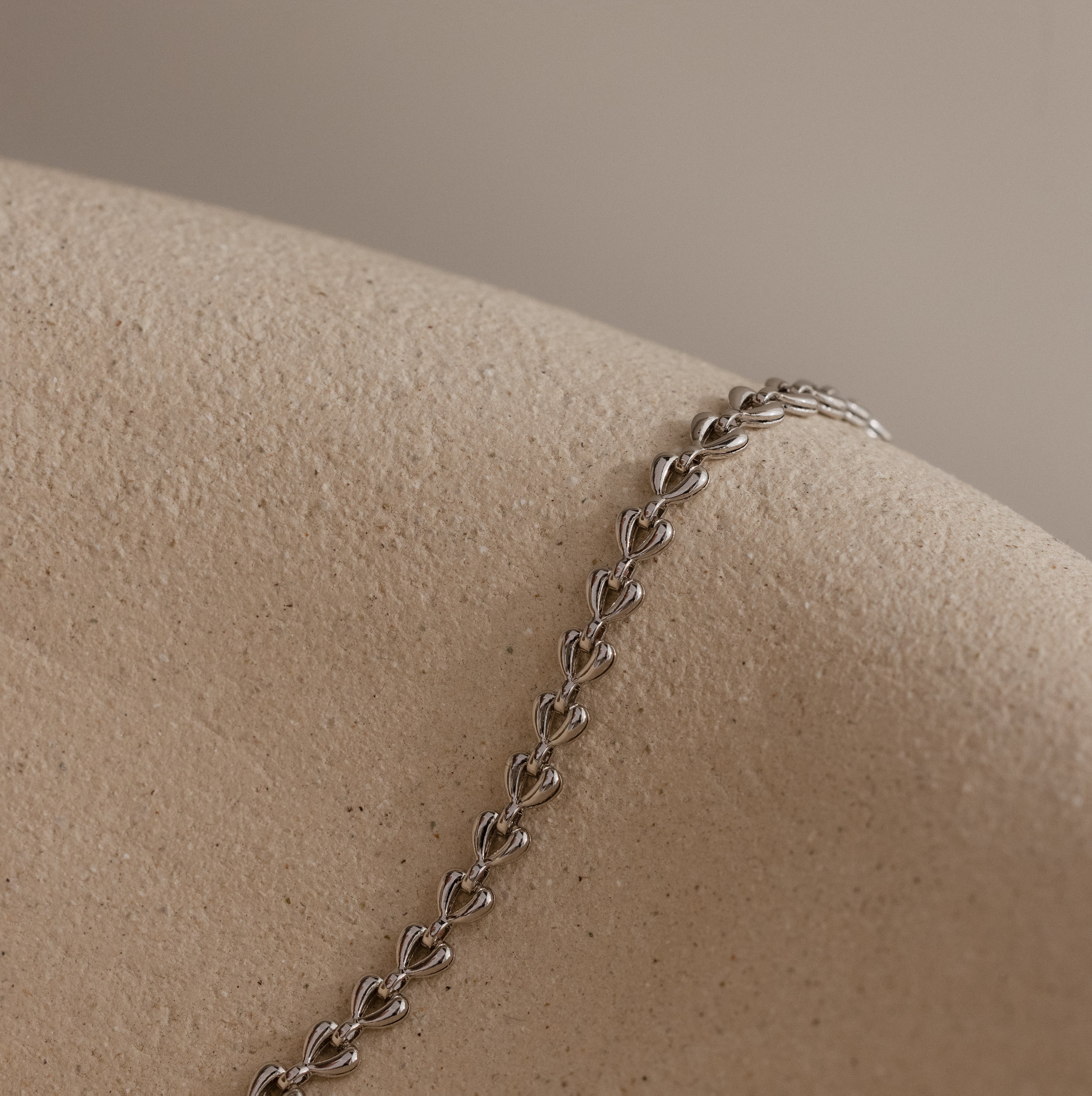 Silver Tiny Link Heart Bracelet draped over a textured ceramic prop.