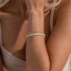 Model wearing a gold Dainty Mirror Chain Bracelet, stacked with a beaded pearl bow charm bracelet.