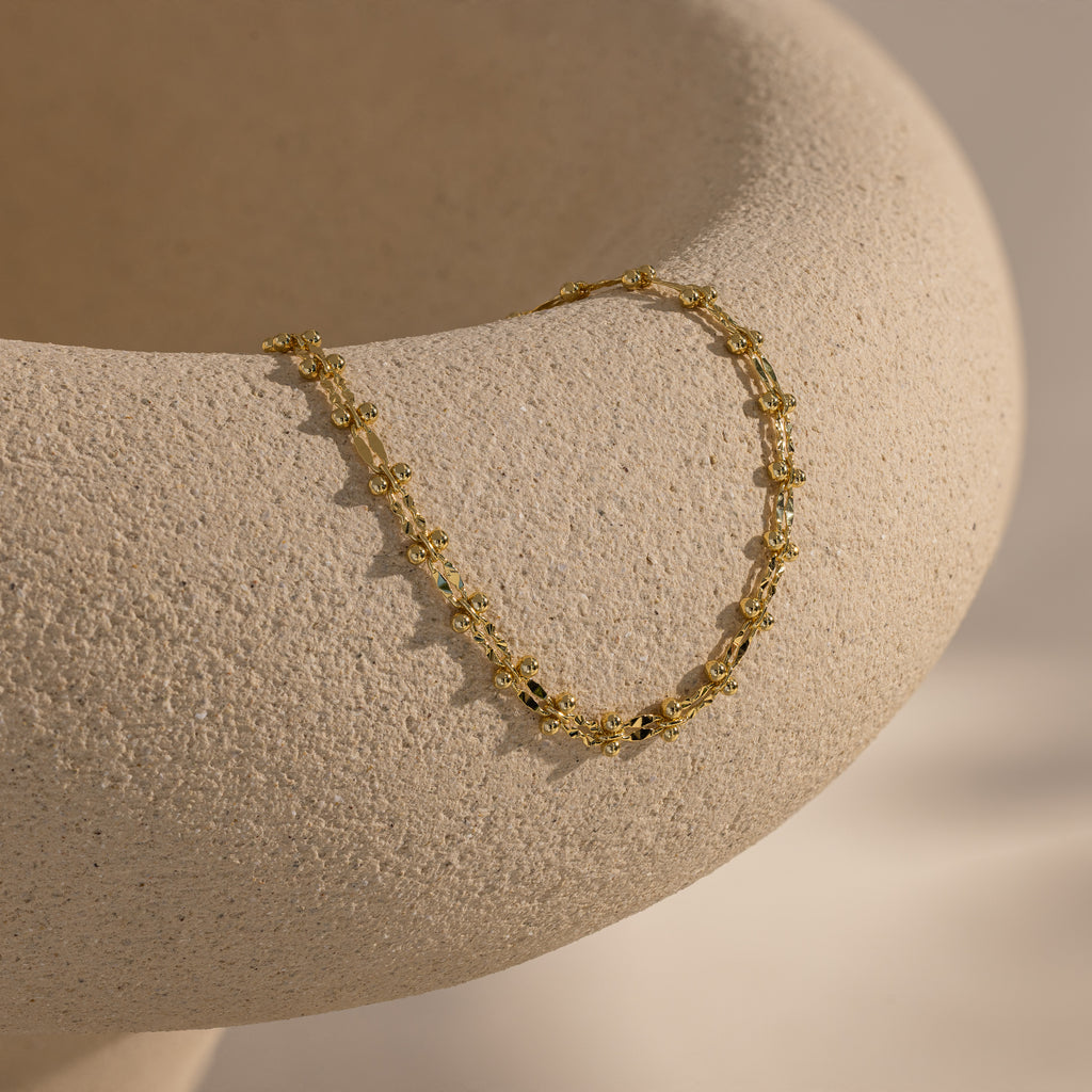 Gold Dainty Mirror Chain Bracelet draped over a textured ceramic surface.