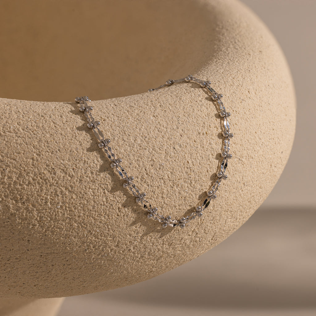 Silver Dainty Mirror Chain Bracelet draped over a textured ceramic surface.