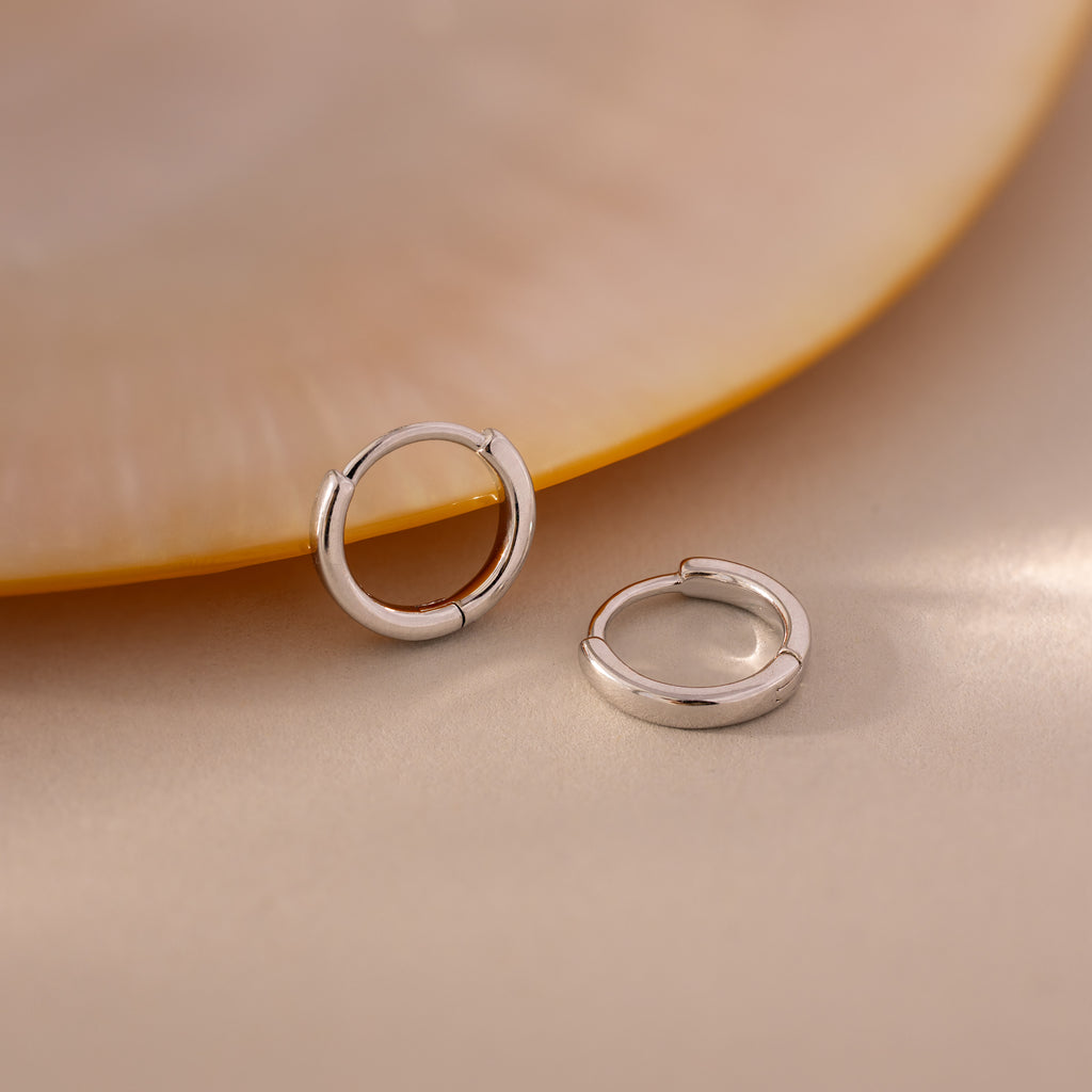 Pair of 7mm silver mini classic huggie hoop earrings displayed on a soft neutral surface.