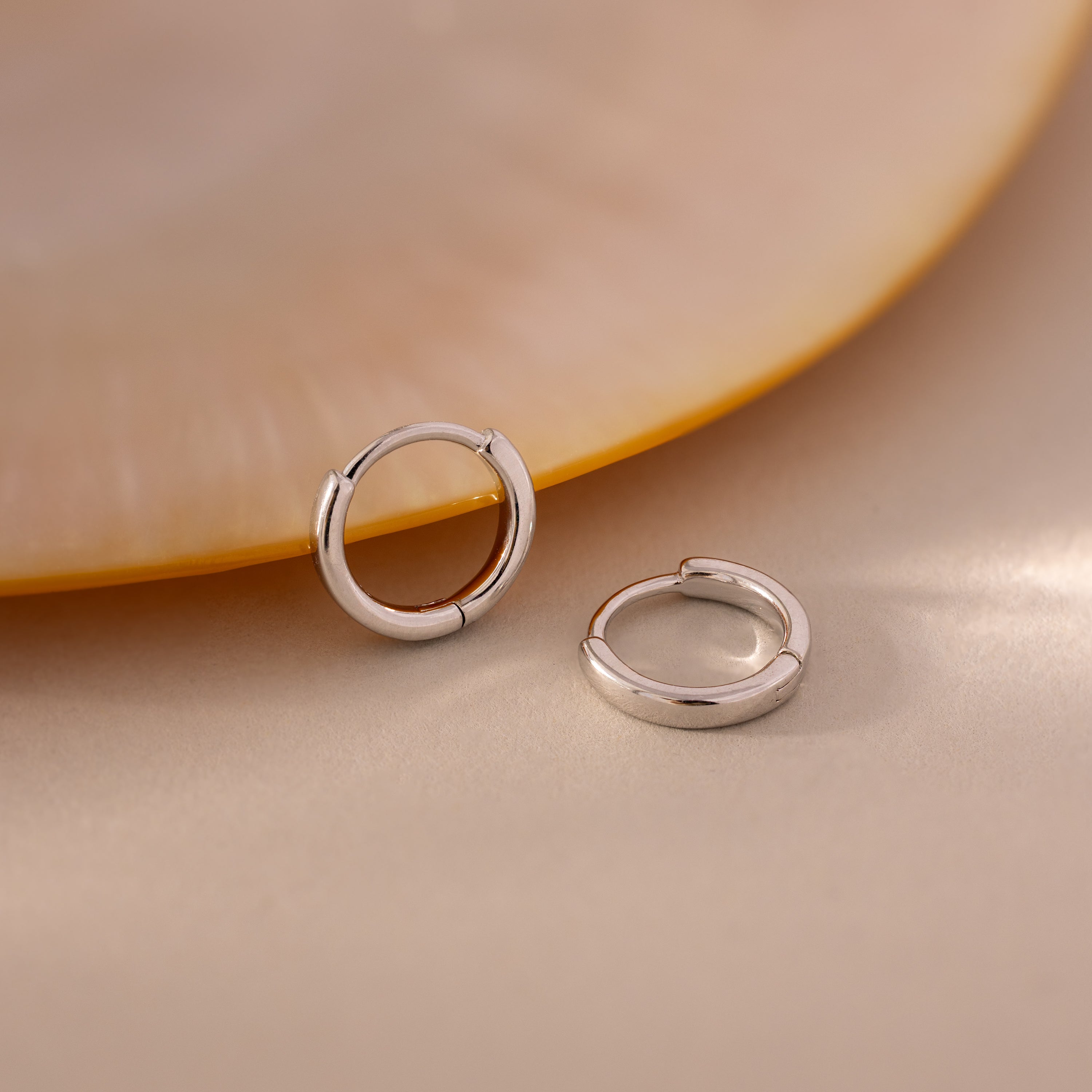 Pair of 7mm silver mini classic huggie hoop earrings displayed on a soft neutral surface.