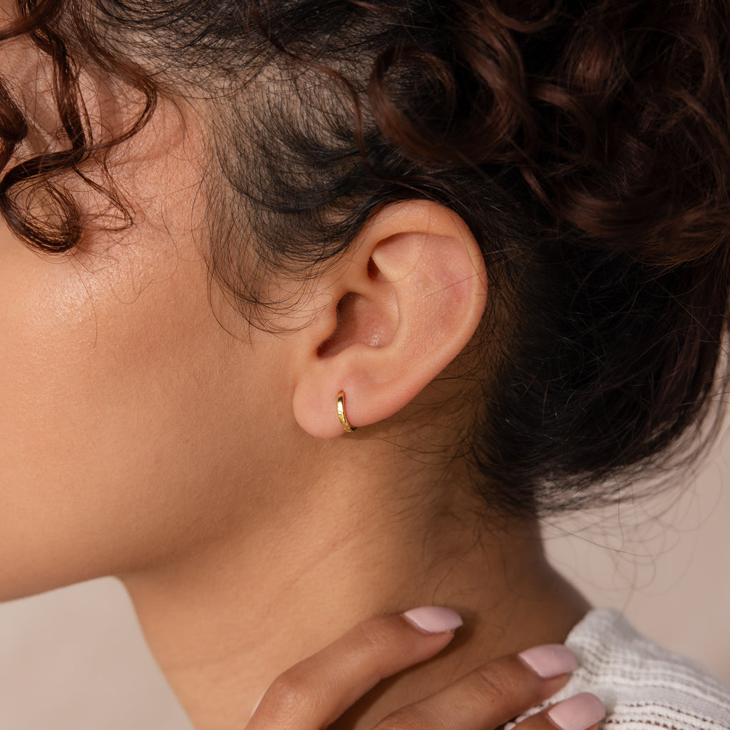 Close-up of model wearing a single 7mm gold mini classic huggie hoop earring styled on the earlobe.