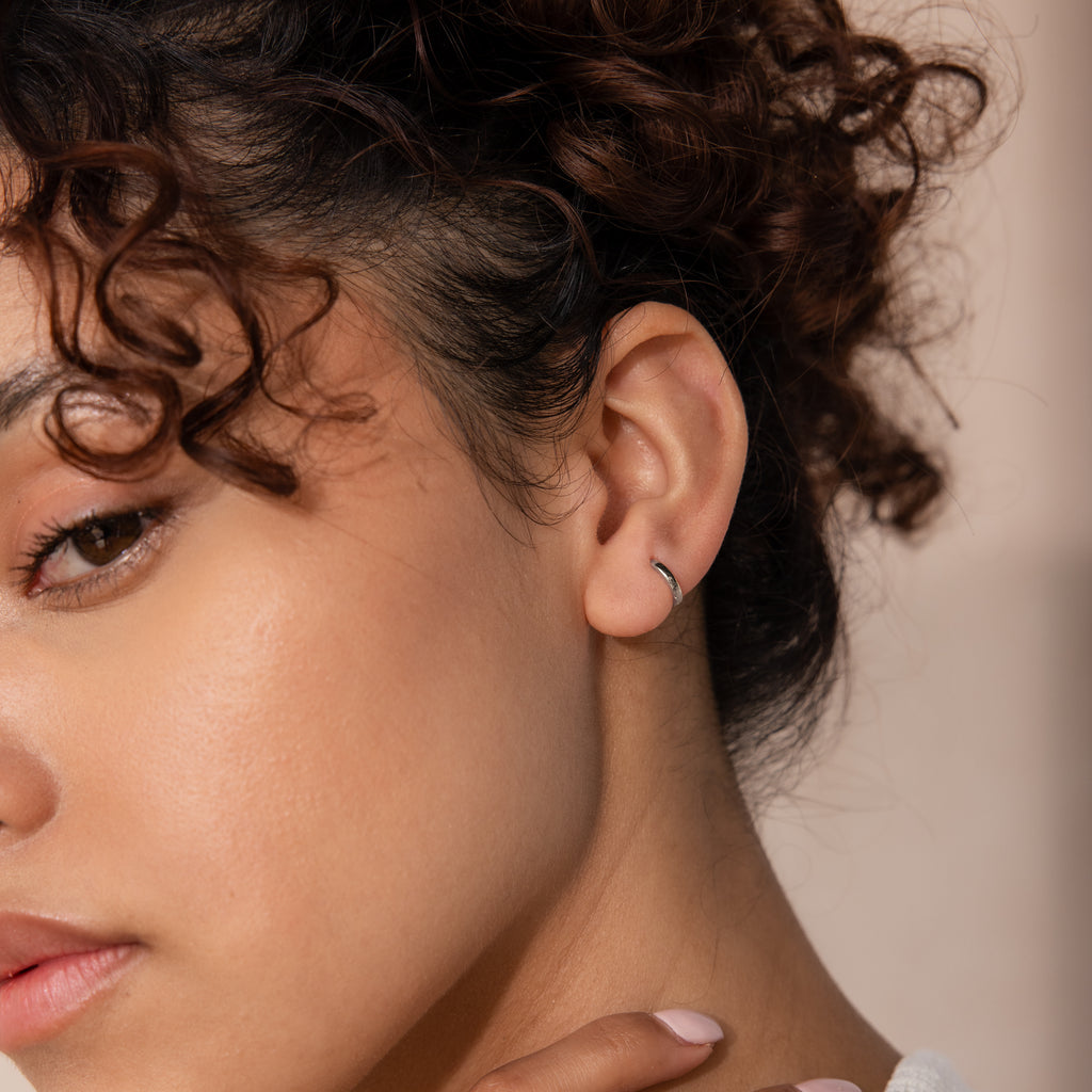 Close-up of model wearing a single 7mm silver mini classic huggie hoop earring.