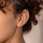 Close-up of model wearing a single 7mm gold mini classic huggie hoop earring.