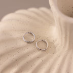 Pair of 8mm small classic silver huggie hoop earrings displayed on a textured ceramic surface.