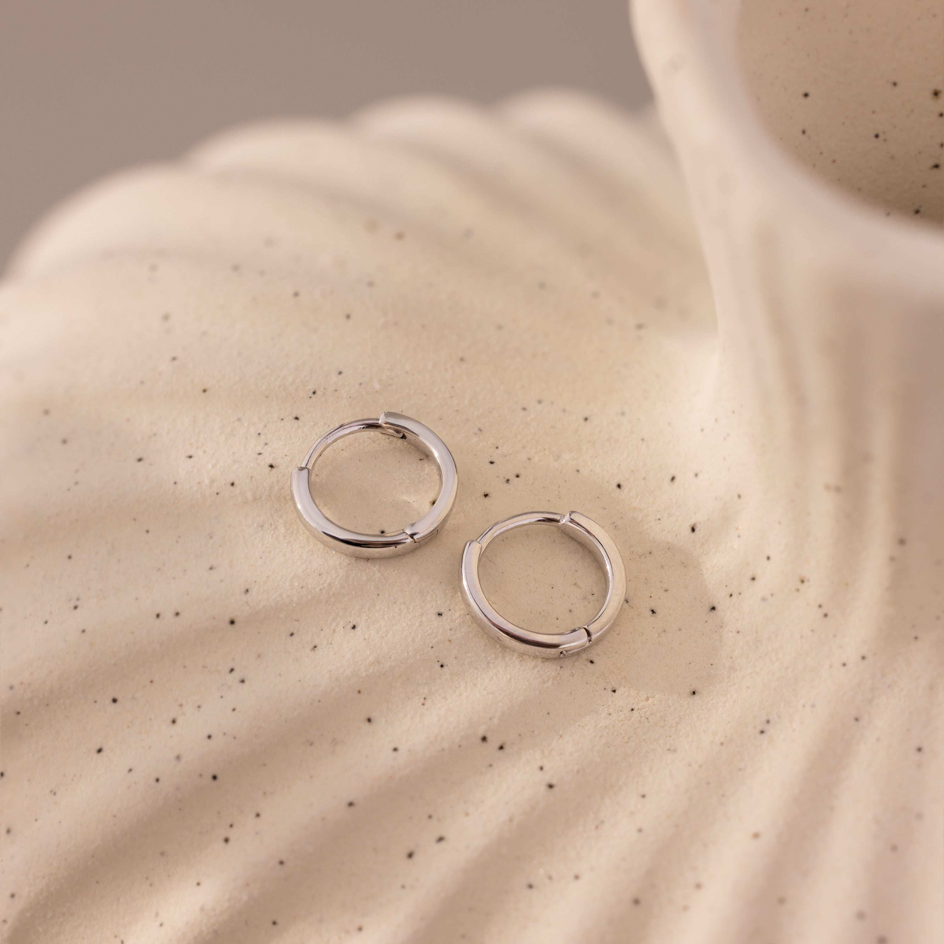 Pair of 8mm small classic silver huggie hoop earrings displayed on a textured ceramic surface.