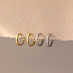 Set of four 8mm huggie hoop earrings in gold and silver finishes, displayed hanging on a textured neutral-toned paper edge.