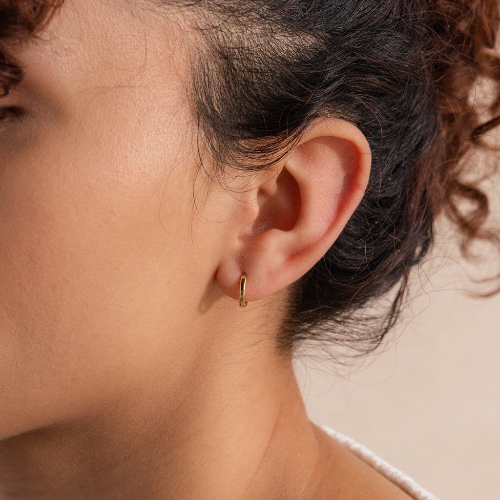 Close-up of model's ear wearing a single 8mm small classic gold huggie hoop earring.