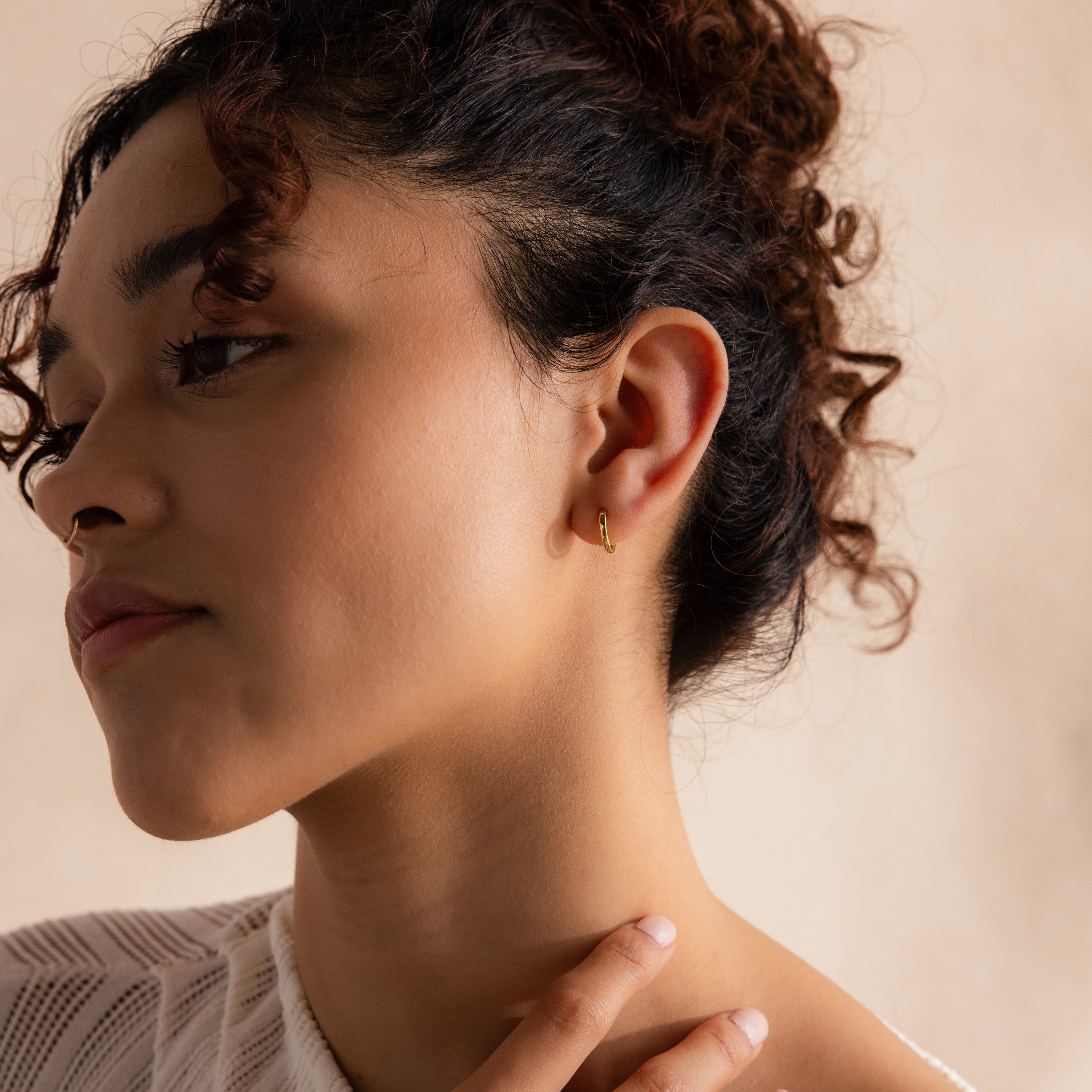 Model wearing a single gold 8mm huggie hoop earring in her lobe, posing with her hand gently touching her collarbone.