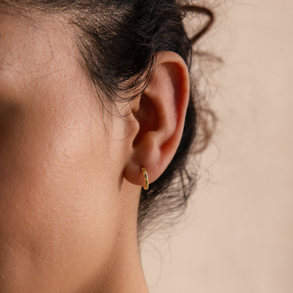 Close-up of a gold 8mm small classic huggie hoop earring worn in model’s first lobe piercing.