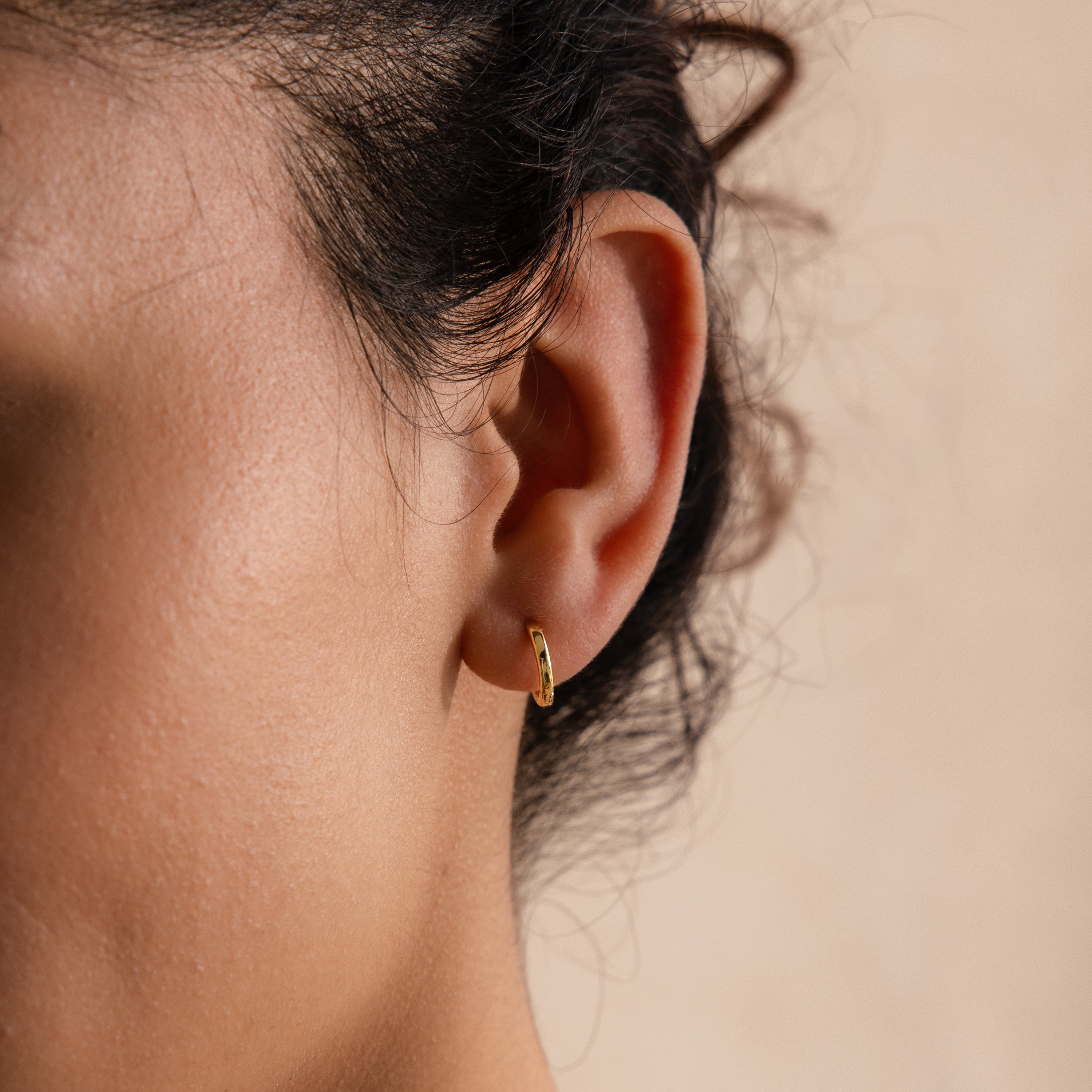 Close-up of a gold 8mm small classic huggie hoop earring worn in model’s first lobe piercing.