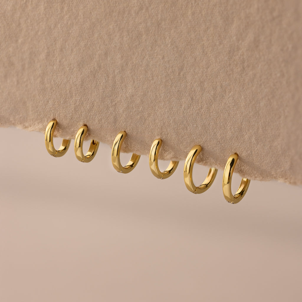 Set of 3 pairs of gold huggie hoop earrings in multiple sizes (6mm to 8mm) displayed on a neutral fabric.