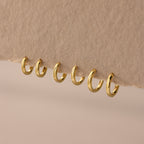 Set of 3 pairs of gold huggie hoop earrings in multiple sizes (6mm to 8mm) displayed on a neutral fabric.