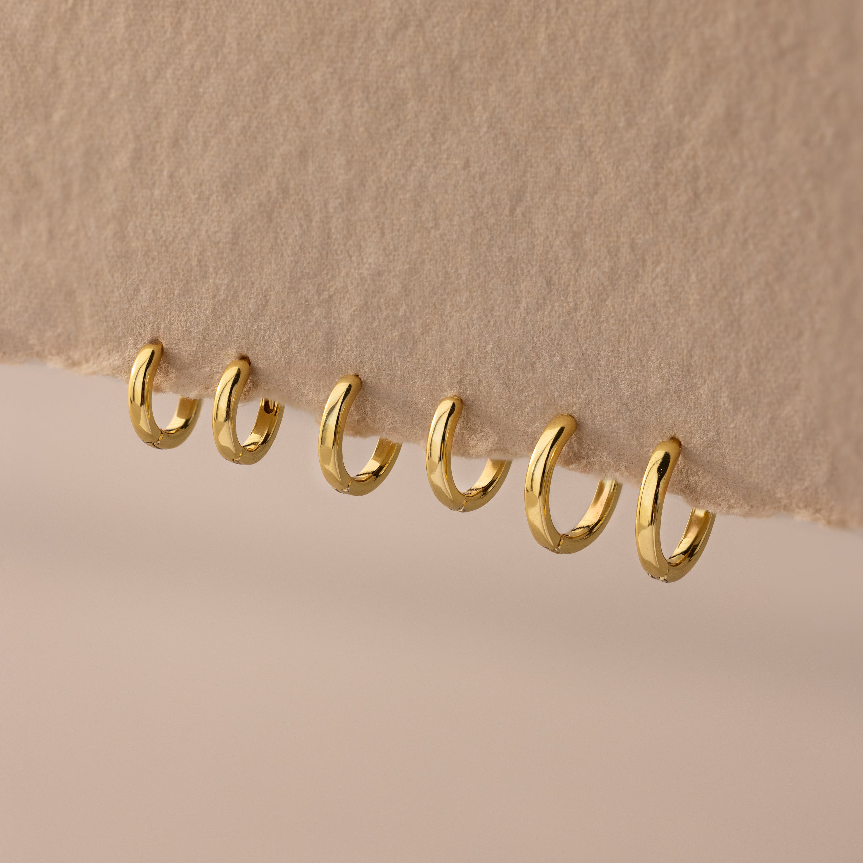 Set of 3 pairs of gold huggie hoop earrings in multiple sizes (6mm to 8mm) displayed on a neutral fabric.