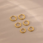 Flat lay of six gold huggie hoop earrings in three different sizes on a soft beige background.