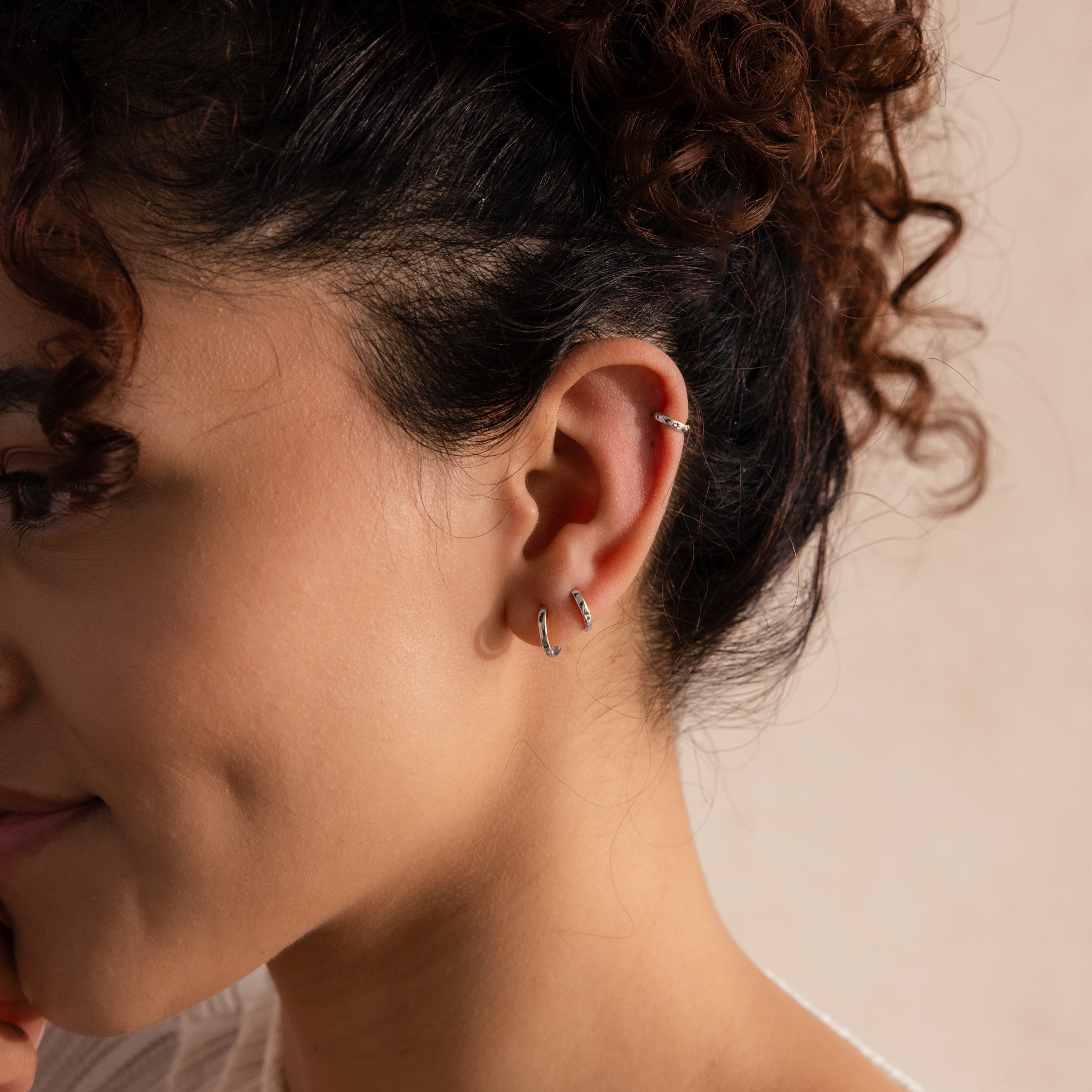 Close-up of model wearing three sizes of dainty silver huggie hoops stacked along her ear.