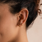 Close-up of model wearing three gold huggie hoop earrings in various sizes, placed on the lobe and helix, under soft lighting.