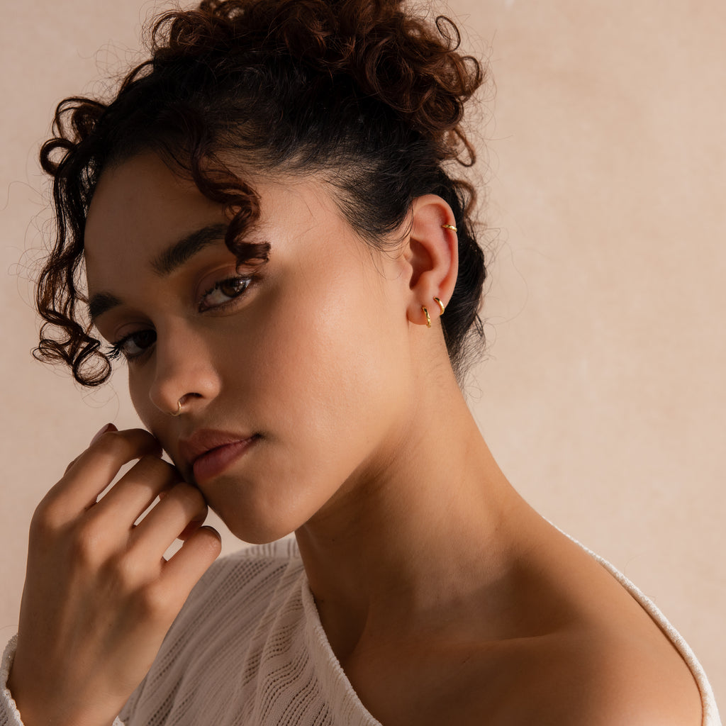 Model showcasing a trio of gold huggie hoop earrings in her cartilage, second, and third lobe piercings.
