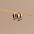 Close-up of a pair of polished silver oval-shaped huggie earrings hanging from a wooden rod.