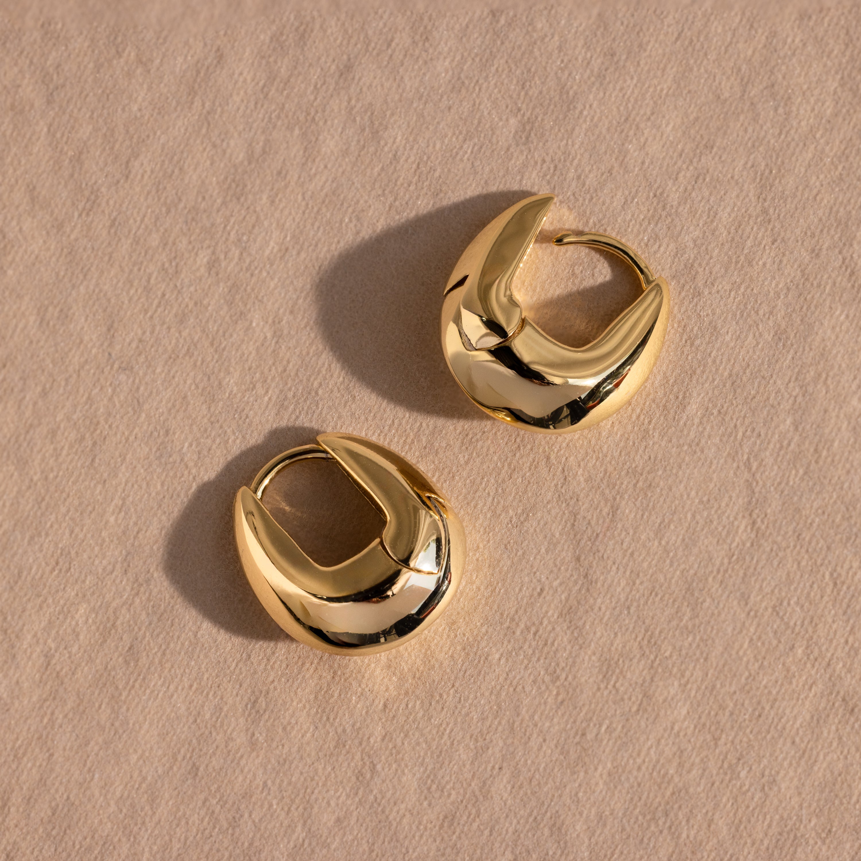 Pair of gold oval-shaped hoop earrings displayed flat on a neutral textured surface.