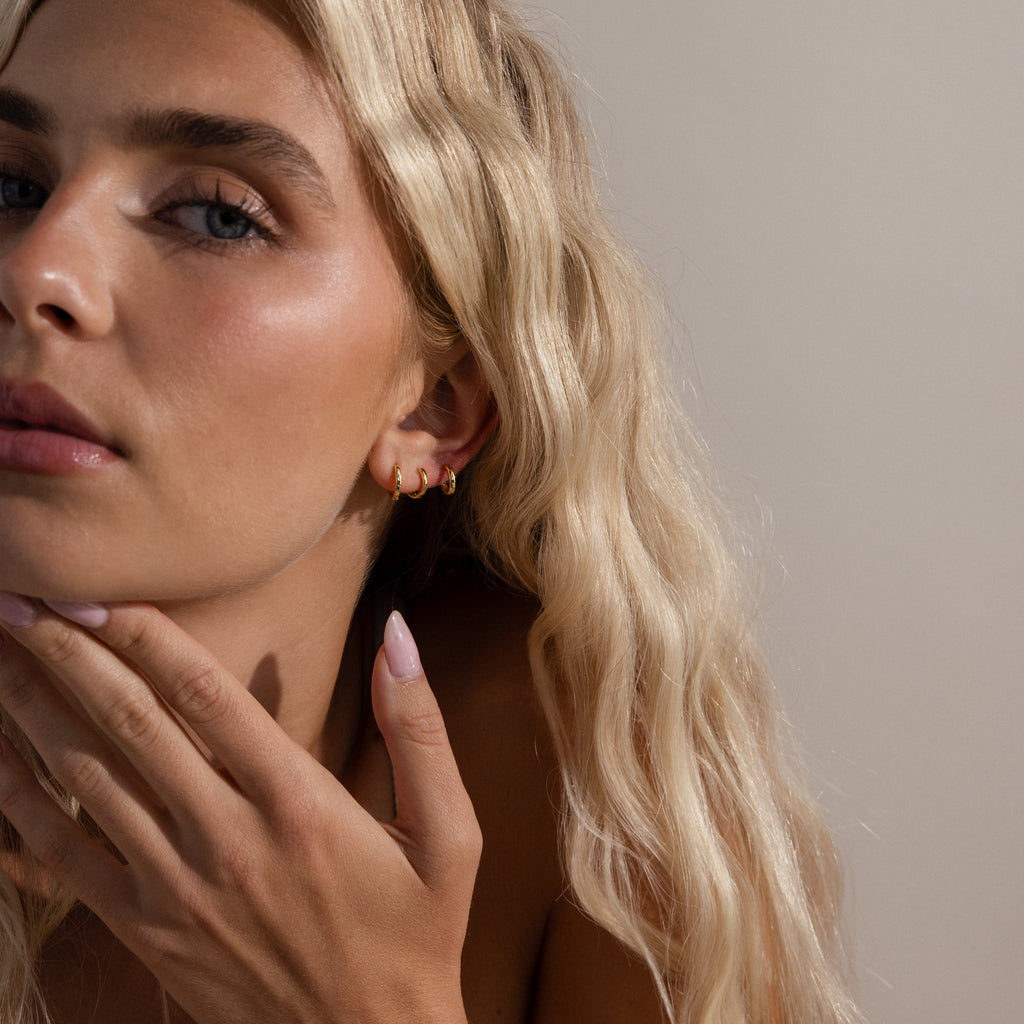 Close-up of model wearing a trio of gold huggie hoop earrings in various sizes on her ear lobe.