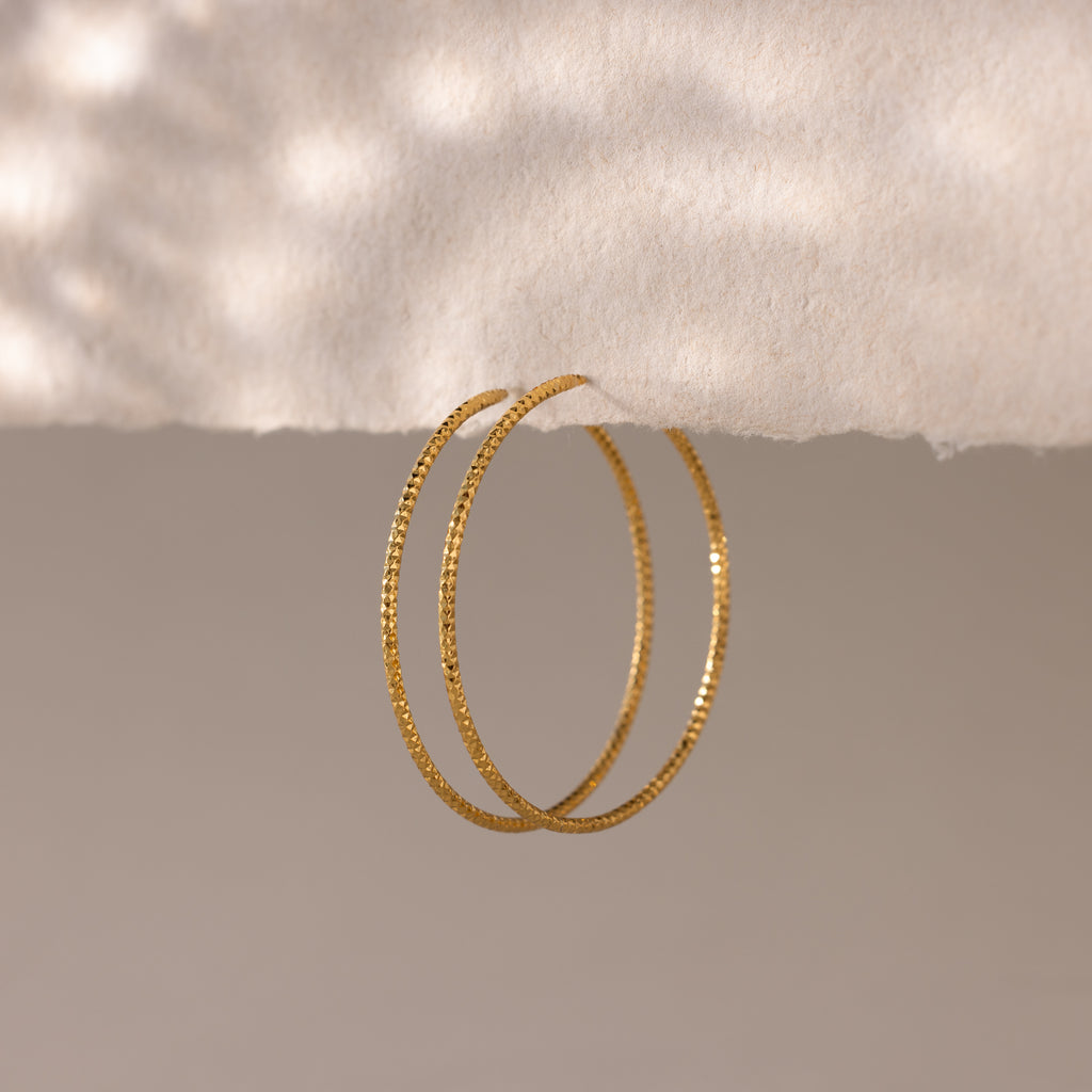 Close-up of finely textured gold hoop earrings suspended elegantly.