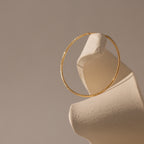 A single gold hoop earring with a refined textured finish, elegantly suspended to highlight its lightweight and radiant design.