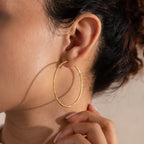Model wearing finely textured gold hoop earrings that catch the light beautifully, highlighting their faceted, high-shine finish.