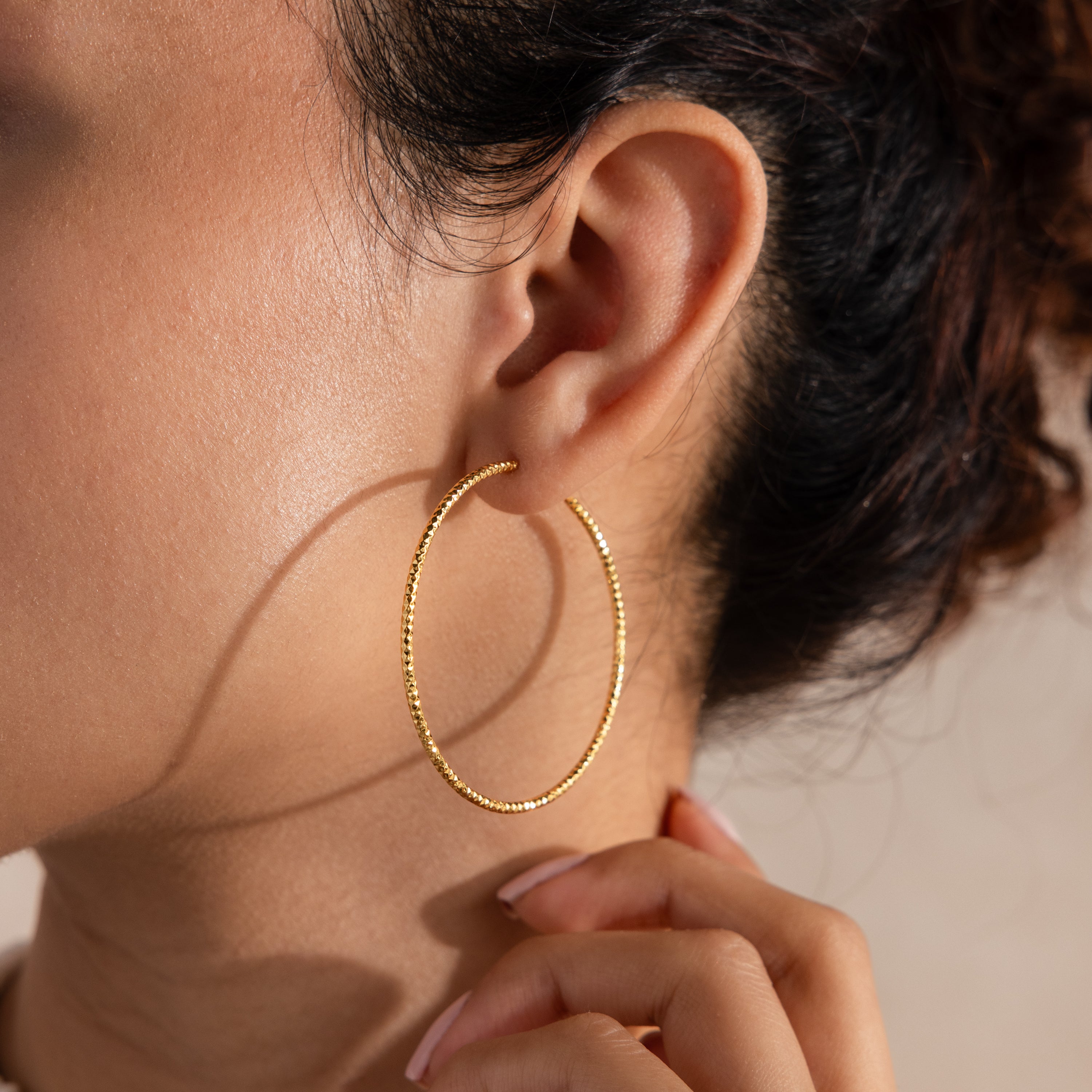 Model wearing finely textured gold hoop earrings that catch the light beautifully, highlighting their faceted, high-shine finish.