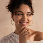 Model wearing large textured gold hoop earrings that catch the light beautifully against a soft, neutral background.