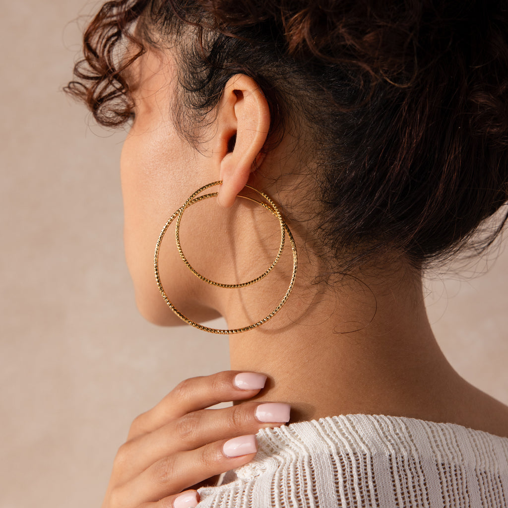 Model wearing oversized double gold hoop earrings with a faceted texture that catches the light beautifully.
