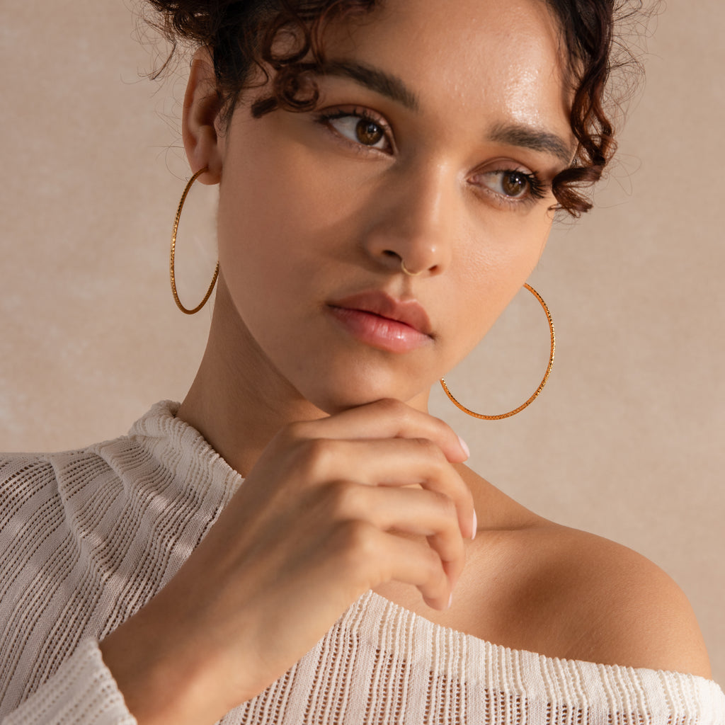 Model wearing large, finely-textured gold hoop earrings that catch the light beautifully.