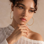 Model wearing large, finely-textured gold hoop earrings that catch the light beautifully.