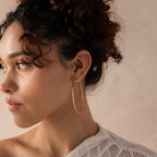 Model wearing large gold hoop earrings with a sleek, textured design, stacked with gold pavé stud earrings.