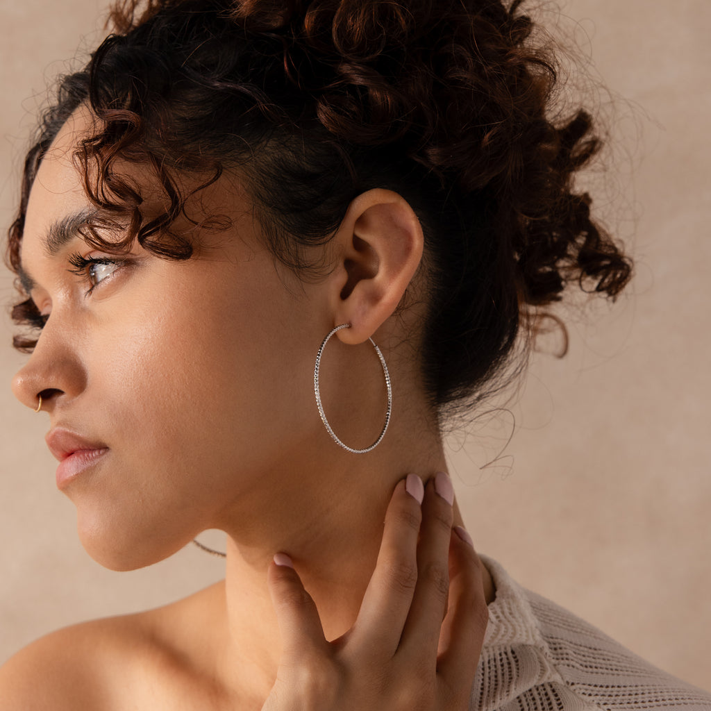 Model wearing a large, silver-toned hoop earring with a faceted, textured finish.
