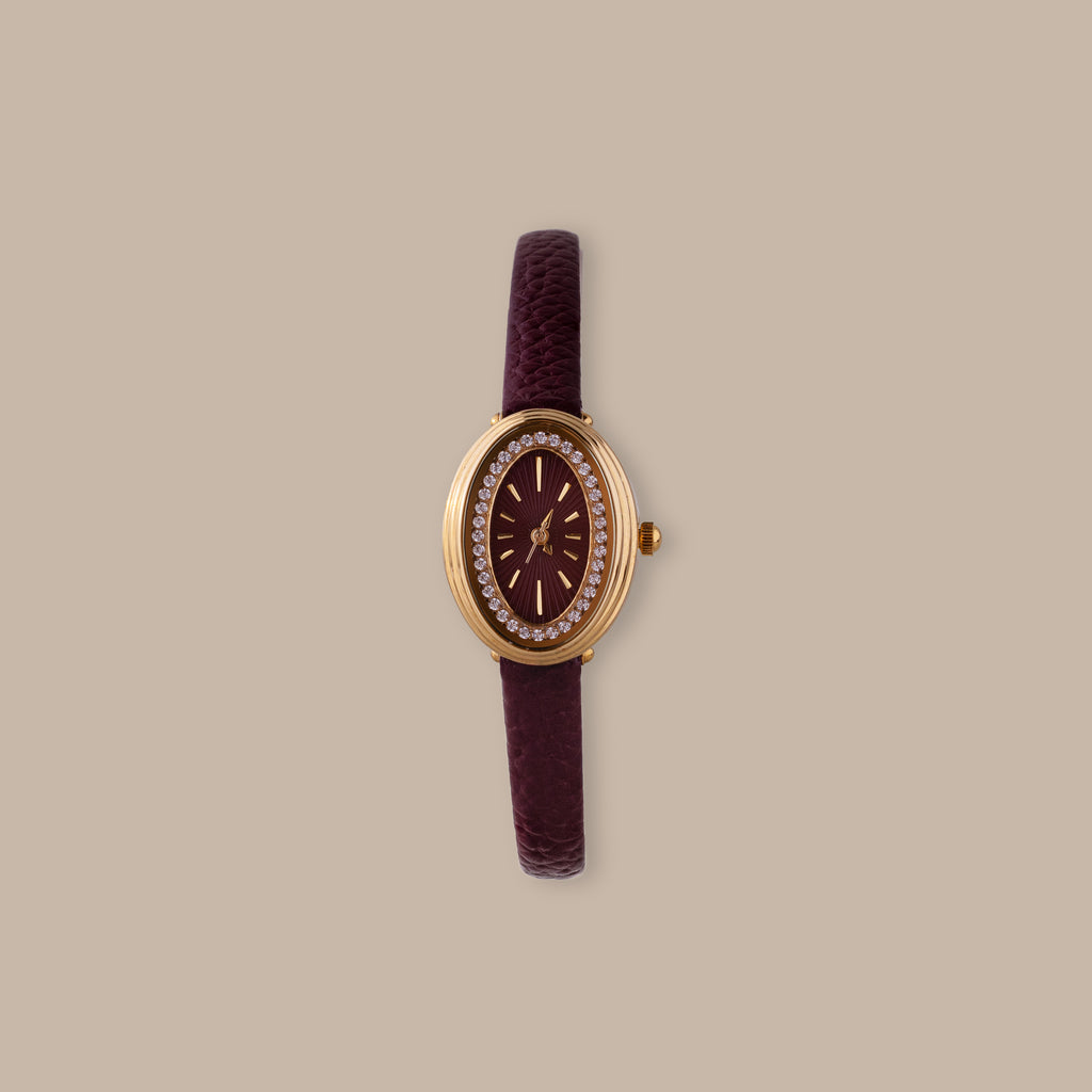 Merlot Strap Timepiece: Gold-tone oval watch with burgundy dial, crystal accents, and textured leather strap.