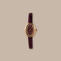 Merlot Strap Timepiece: Gold-tone oval watch with burgundy dial, crystal accents, and textured leather strap.