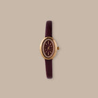 Merlot Strap Timepiece: Gold-tone oval watch with burgundy dial, crystal accents, and textured leather strap.