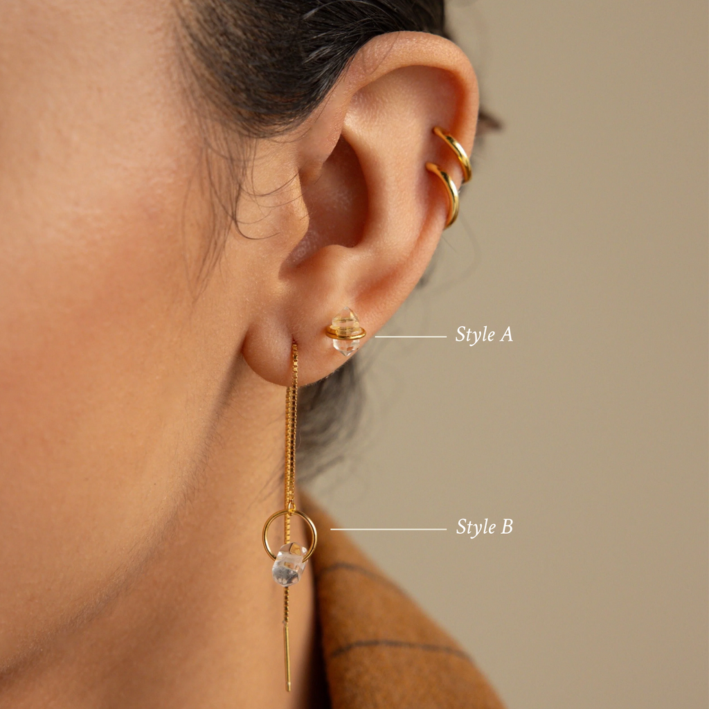 Close-up of an ear wearing three gold earrings, including studs and a dangling chain, with one pair featuring the sparkling Herkimer Diamond Earrings.