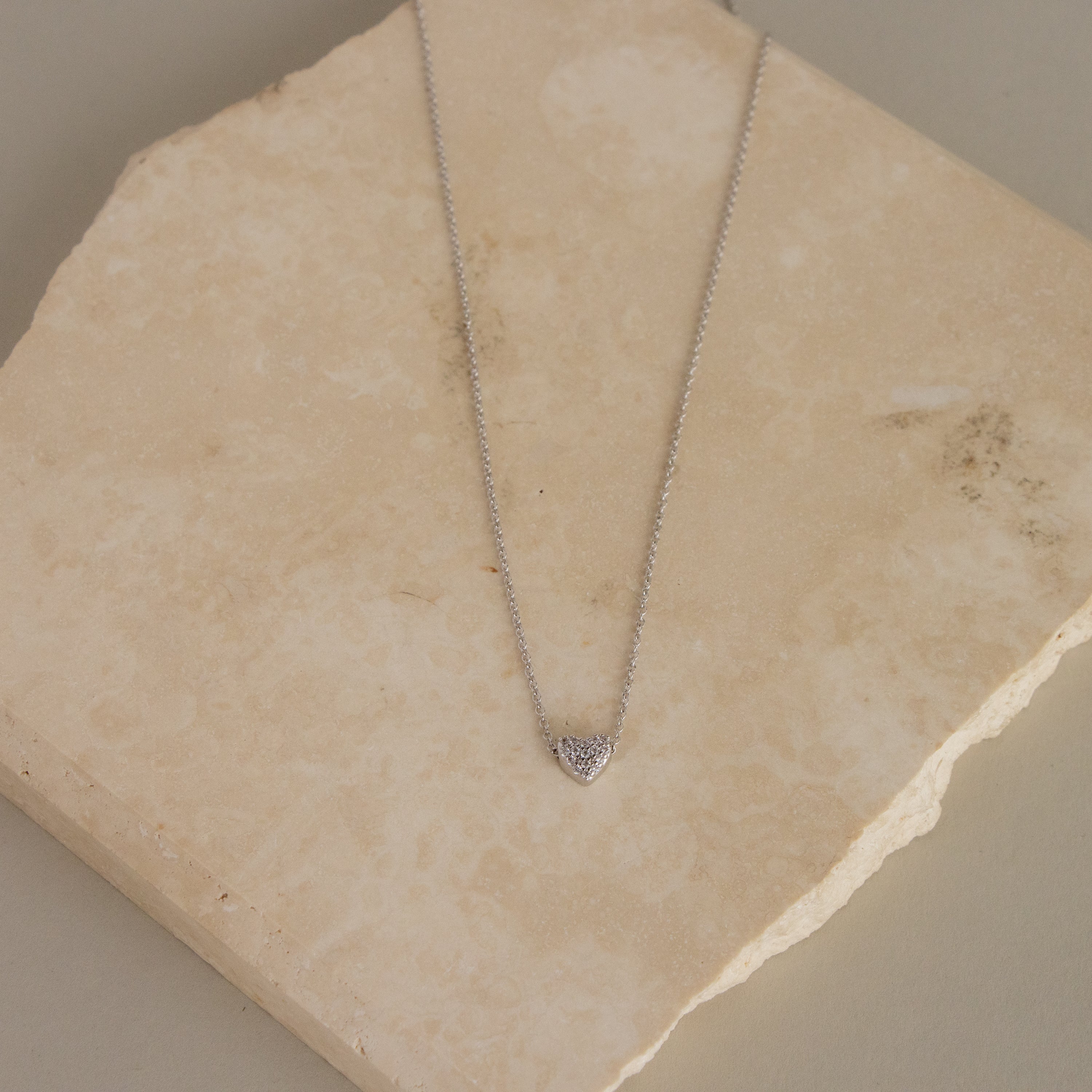 Silver Pave Heart Charm Necklace shown on a square beige stone slab.