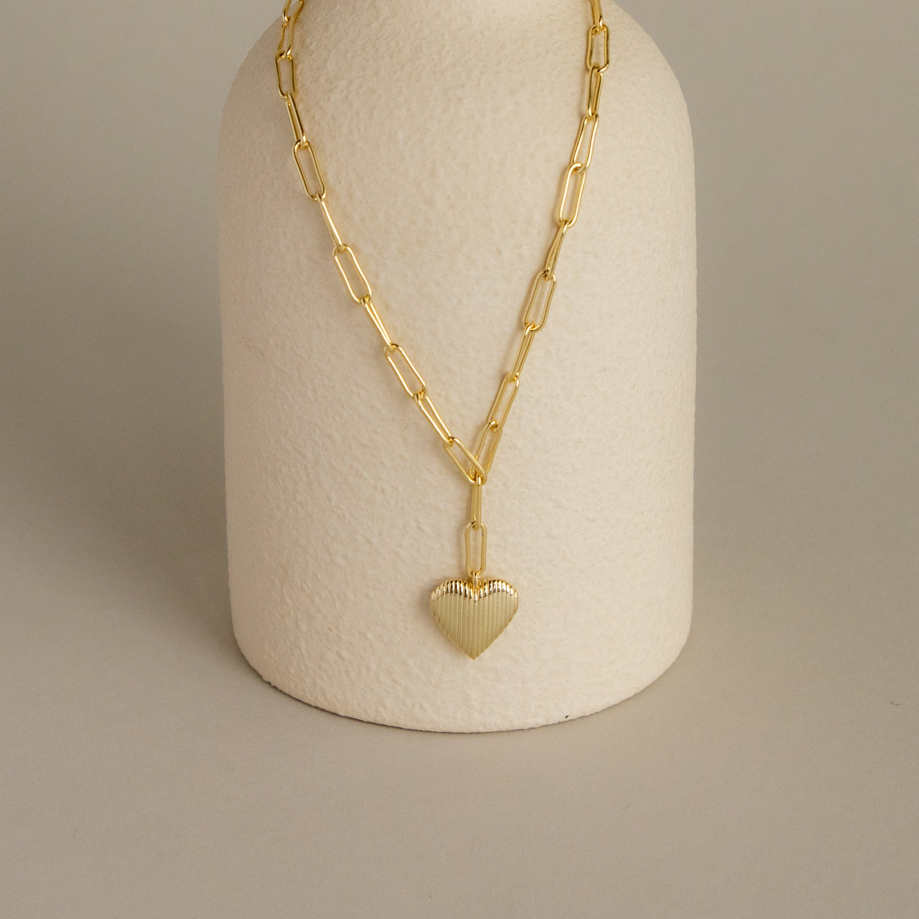 Fluted Heart Paperclip Pendant Necklace featuring a textured heart pendant, displayed on a cream textured stand.