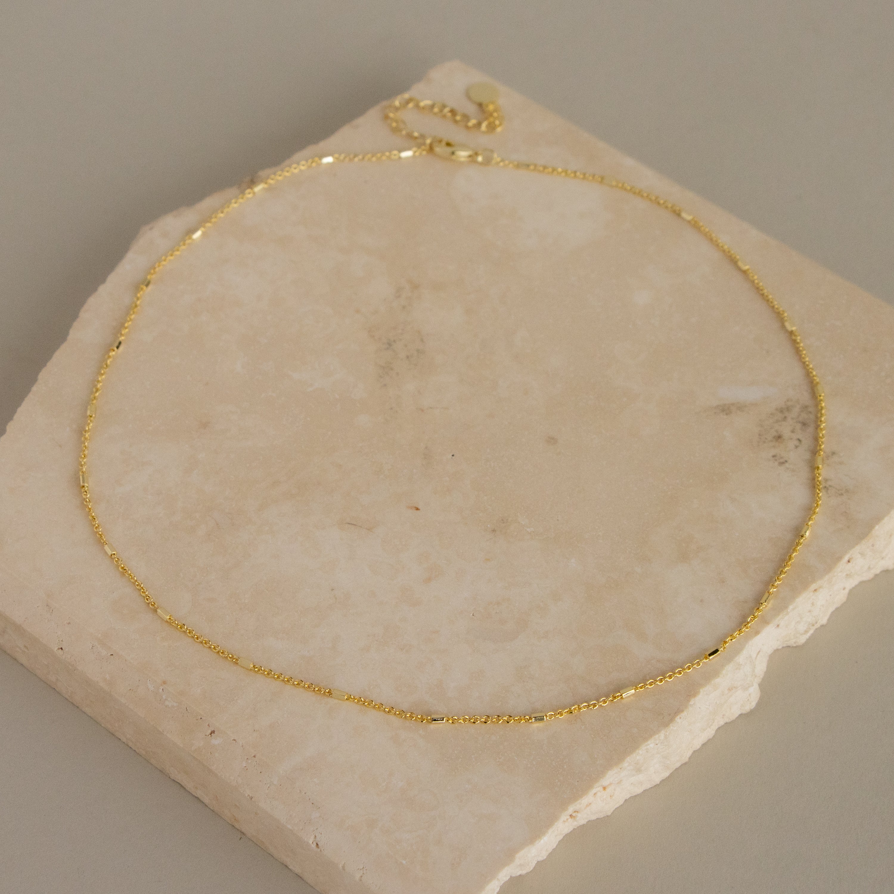 The Mini Bar Cable Chain Necklace is displayed on a square beige stone tile.