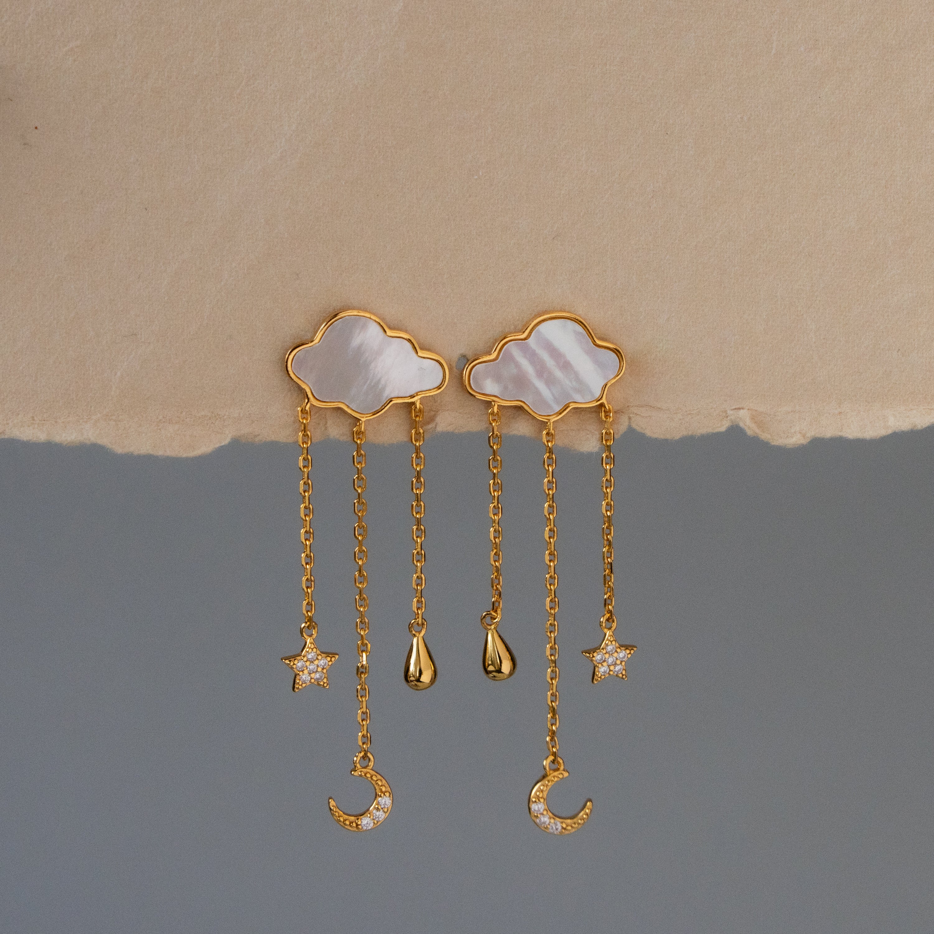 Celestial Pearl Cloud Chain Drop Studs featuring gold clouds with dangling star, moon, and raindrop charms, showcased on a neutral background.