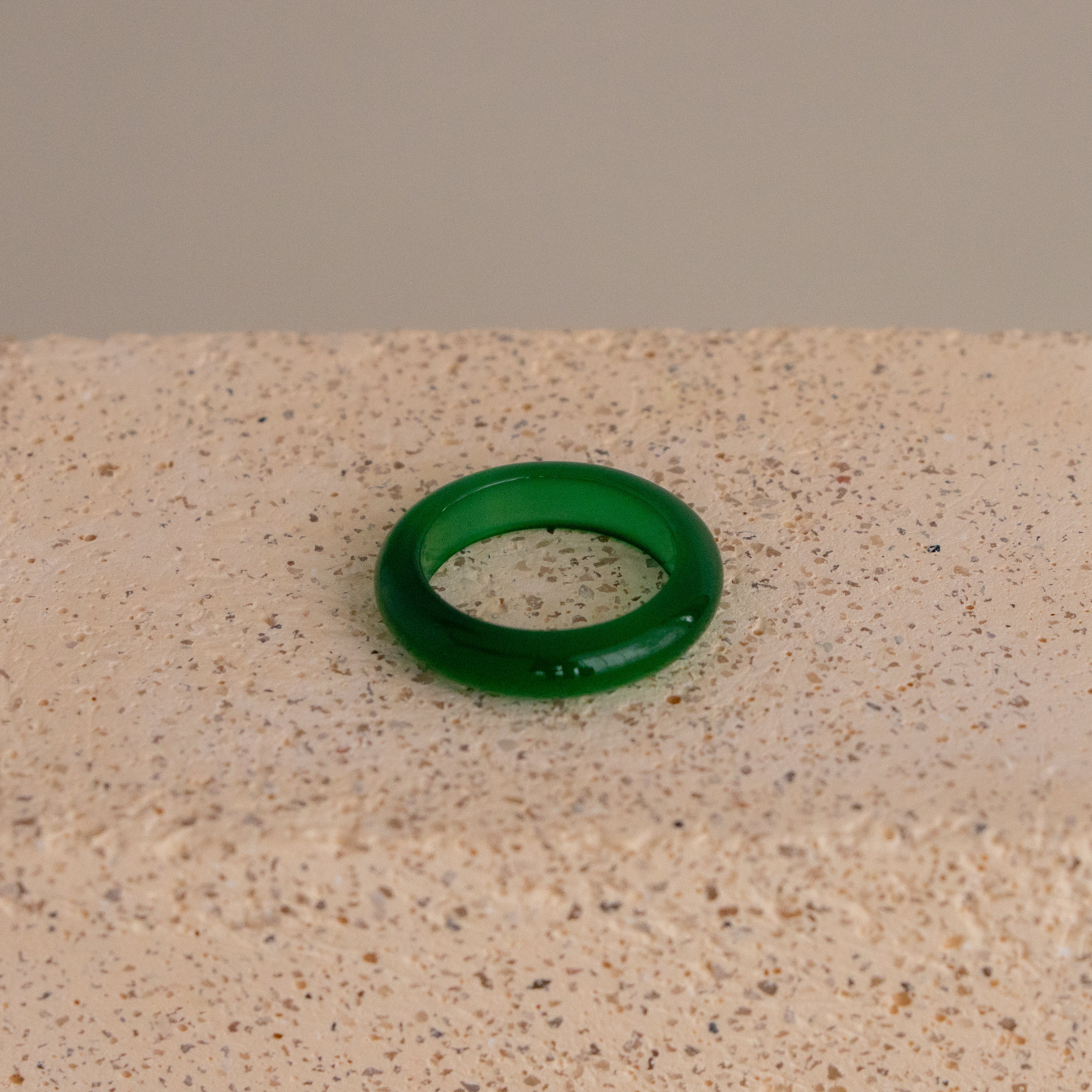 The Green Halo Ring, featuring a green translucent design, rests on a textured beige surface.