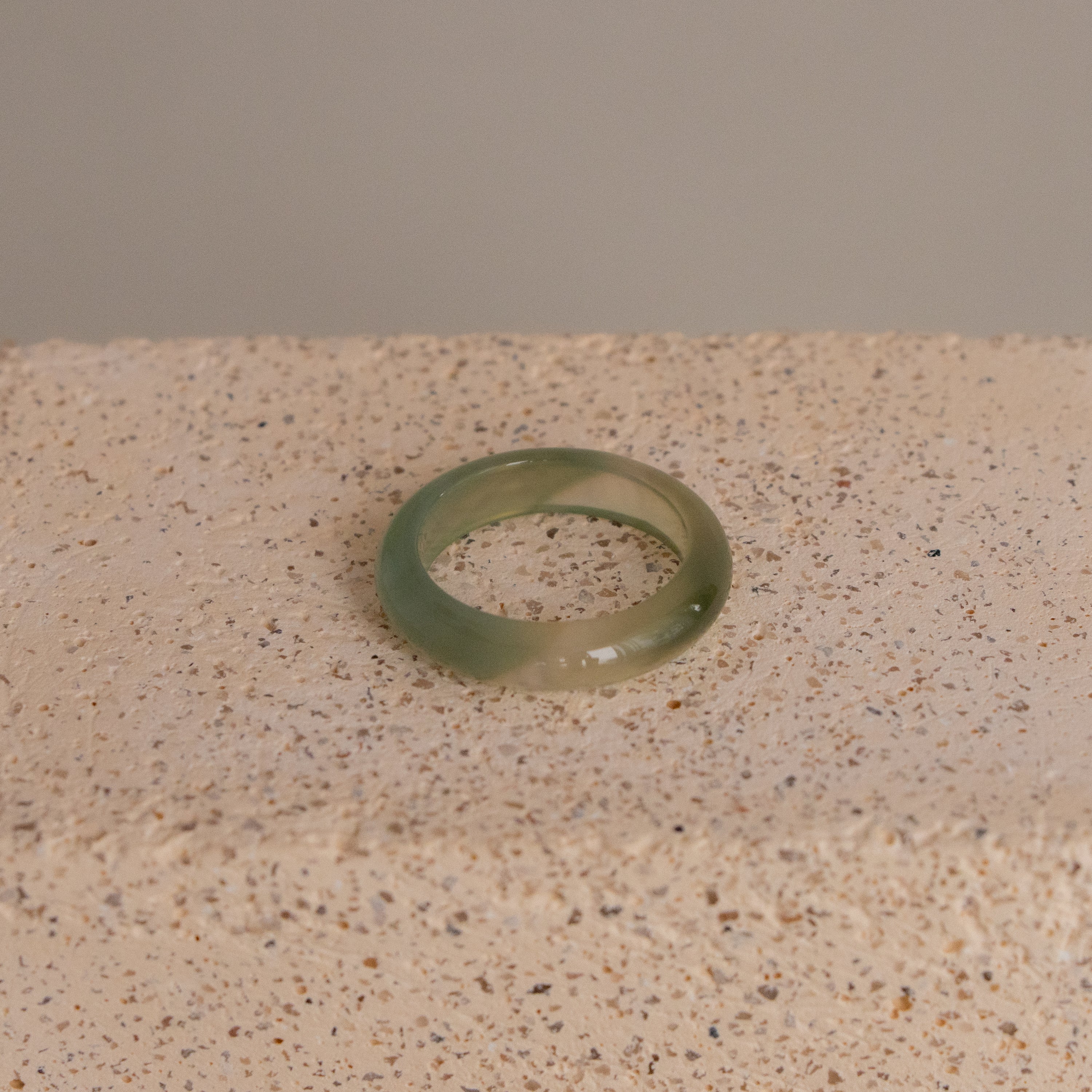 A Light Green Chalcedony Halo Ring displayed on a textured beige surface.