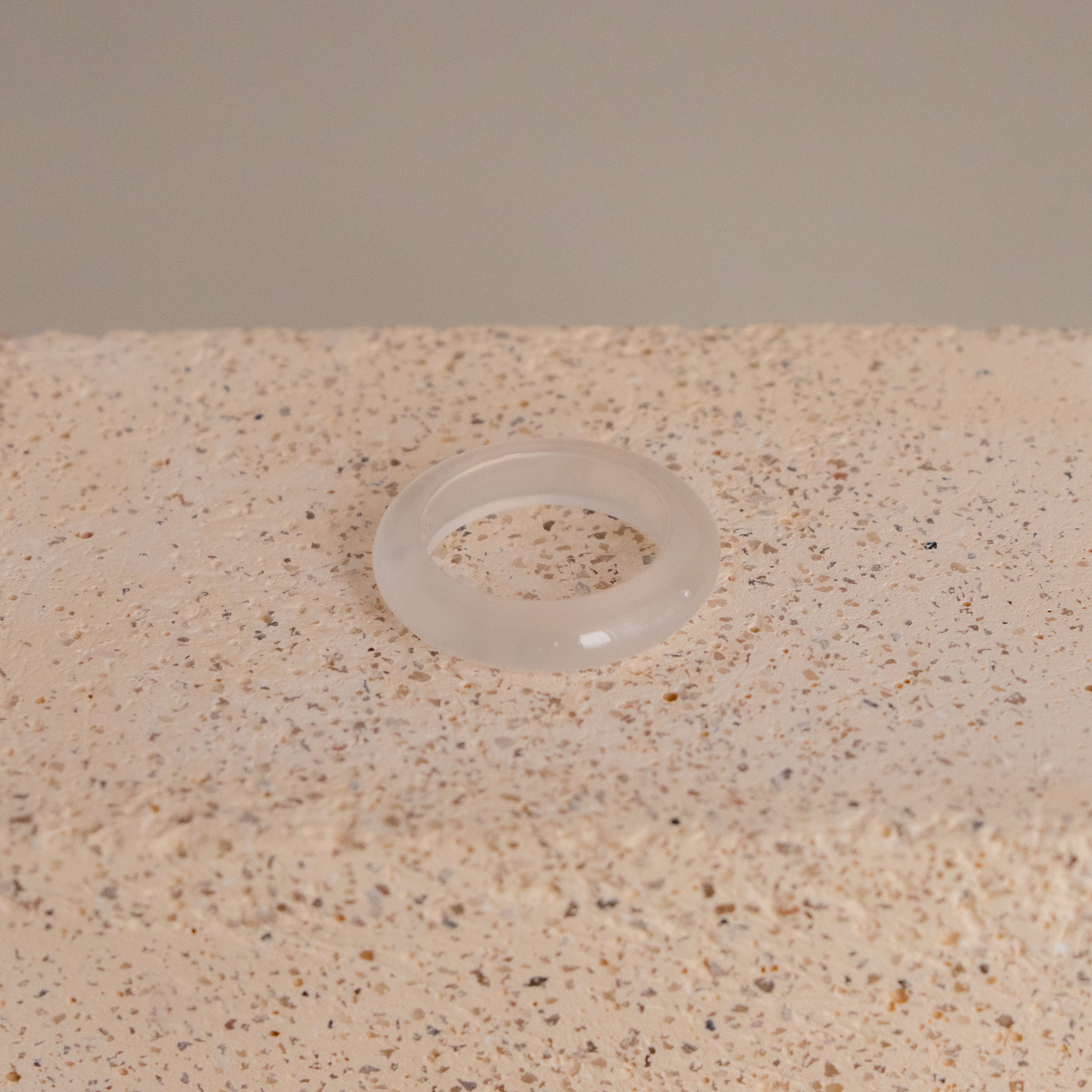A White Halo Ring made of translucent silicone rests on a textured beige surface.