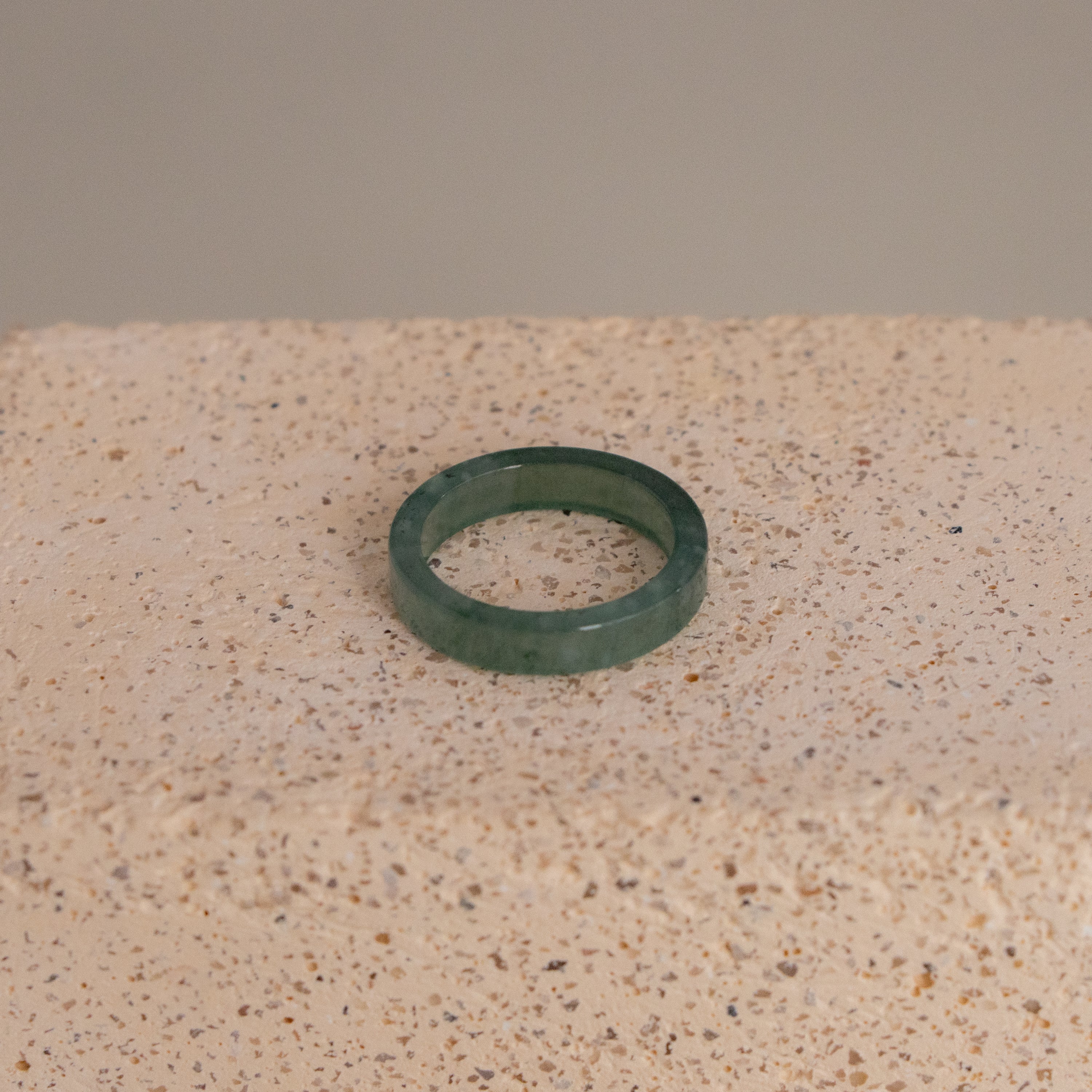 The Zen Jade Ring is displayed resting on a textured beige stone surface.