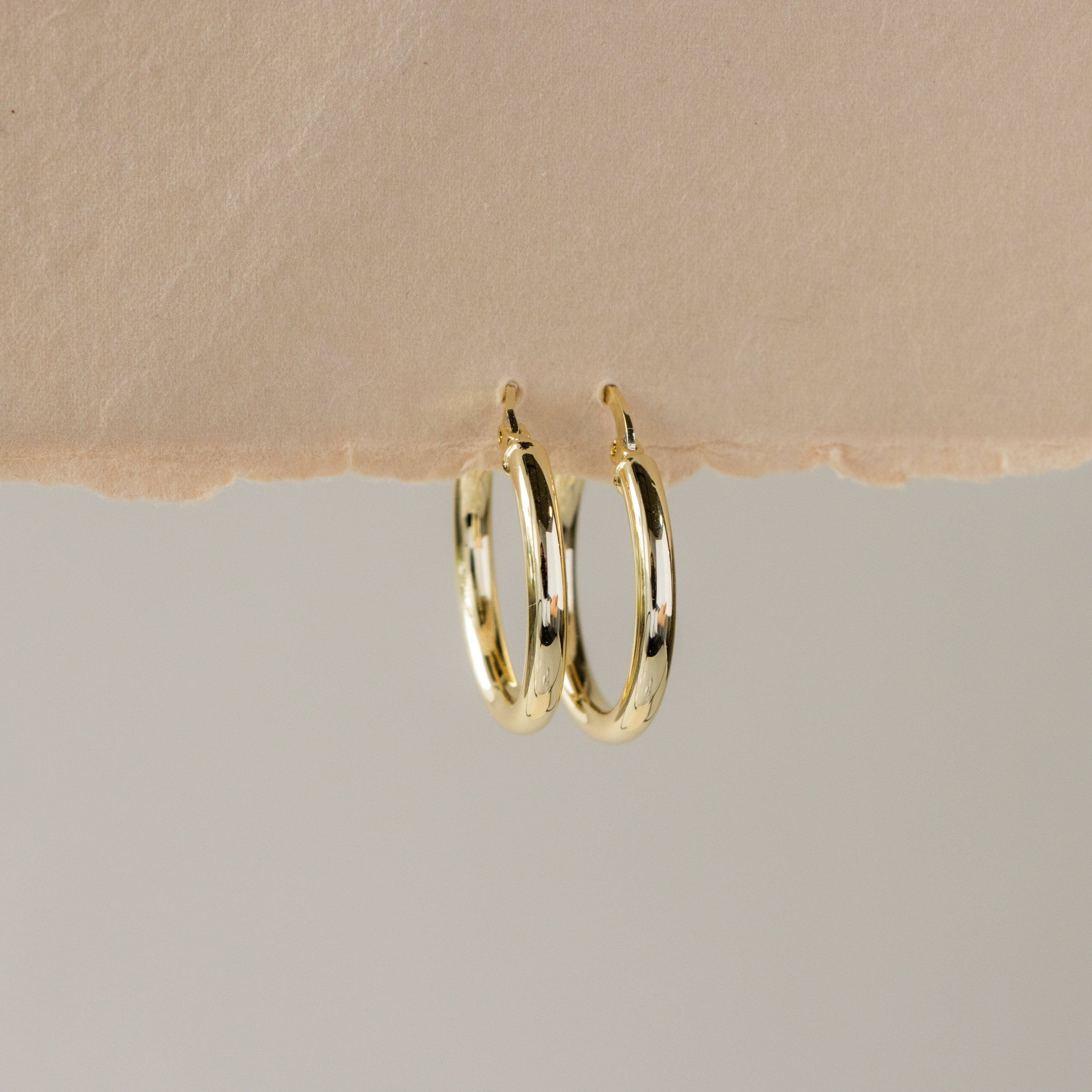 Medium Latchback Hoops displayed on the edge of textured beige paper with a neutral background.
