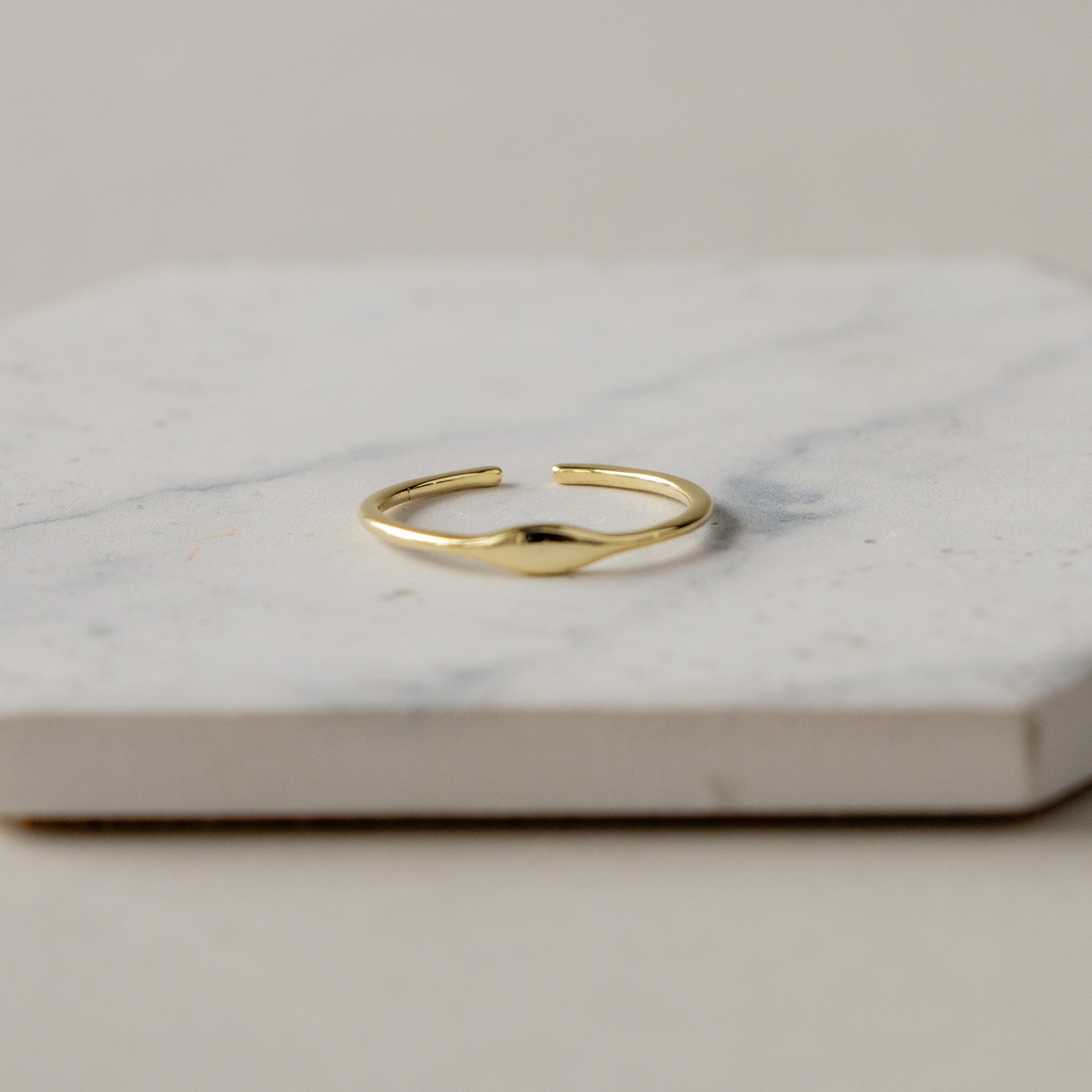 The Dainty Open Signet Ring is displayed on a white marble surface with a neutral background.